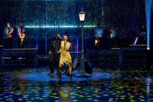 Musiker auf beleuchteter Bühne mit Band im Hintergrund.