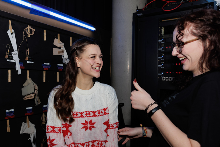 Zwei Frauen lachen hinter der Bühne neben Technikschrank
