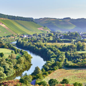 Landschaft mit Fluss, Wäldern und Hügeln im Hintergrund.