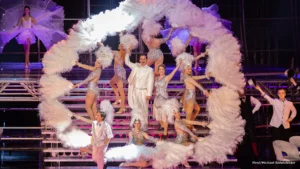 Tänzer in glamourösen Kostümen auf Showbühne mit Federn.